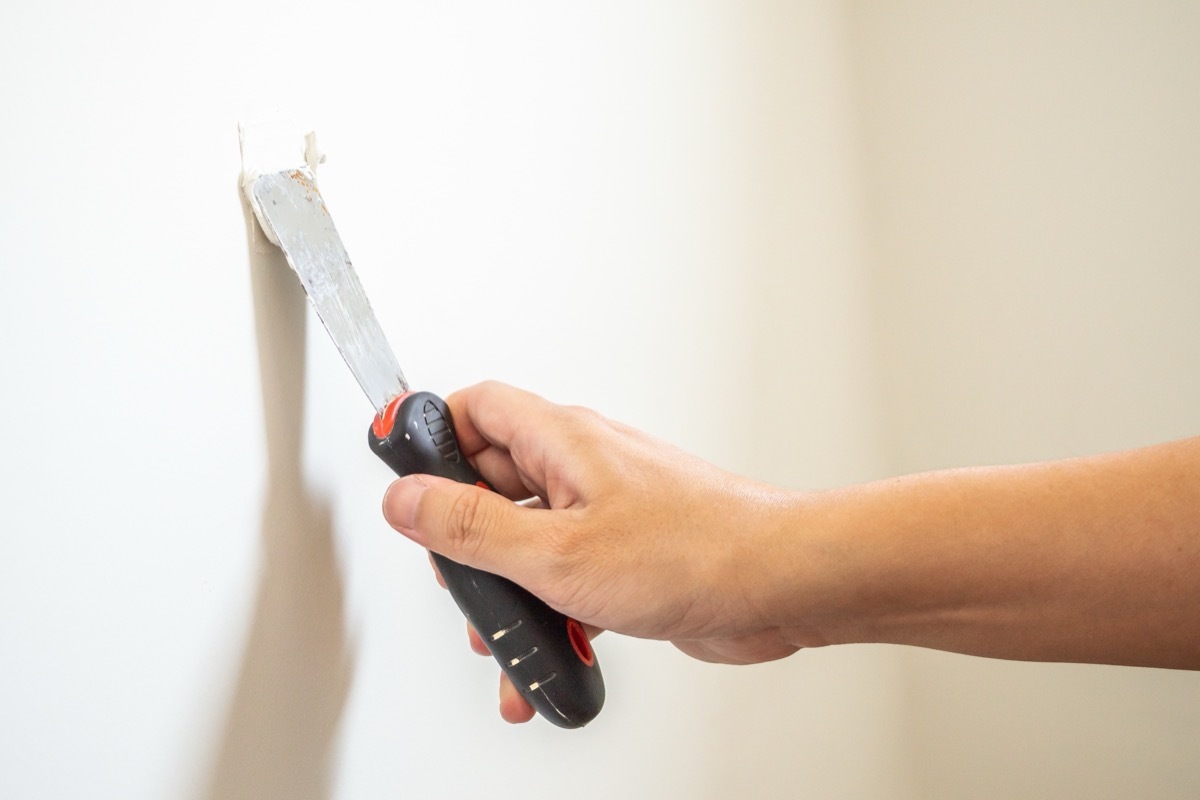 Person sealing a hole in a white wall. 