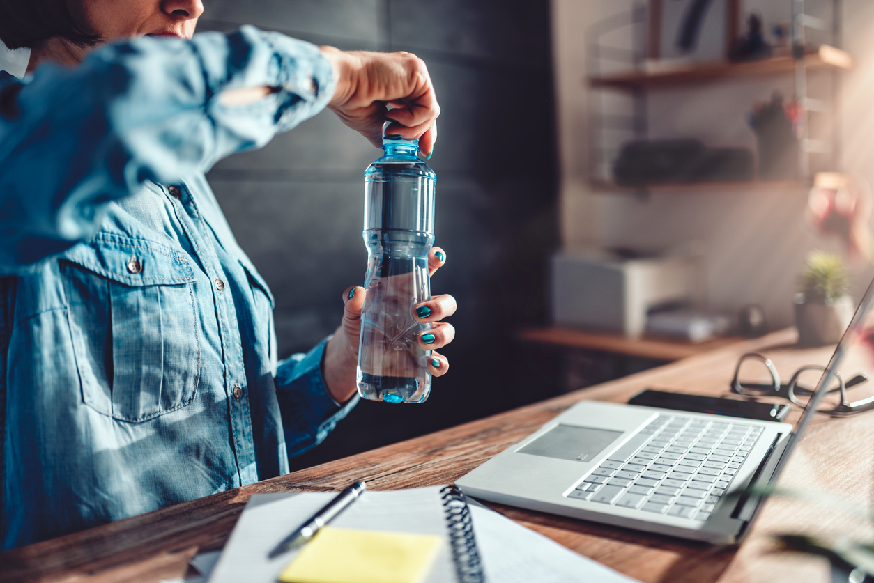 Woman wearing denim shirt working in the office and opening plastic bottle of water