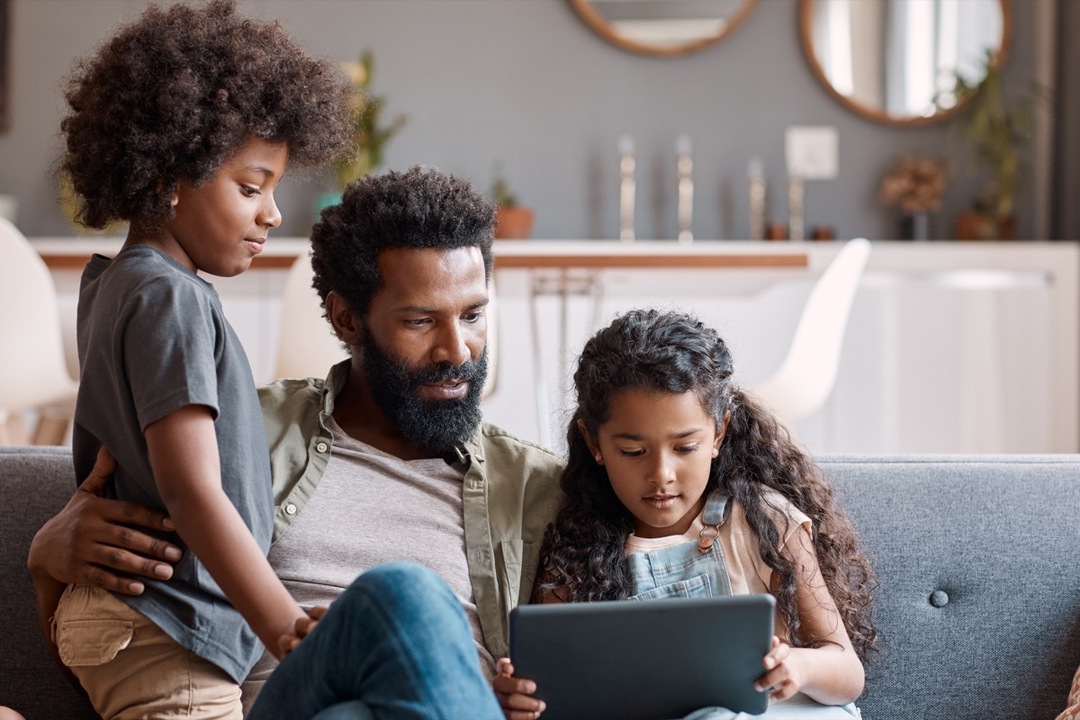 Shot of two adorable young siblings using a digital tablet while bonding and relaxing with their father at home