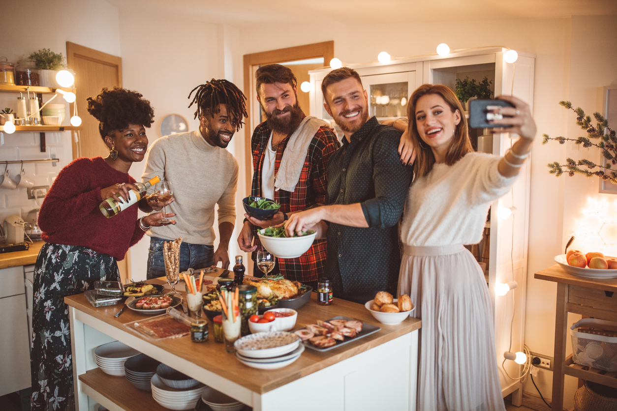 A group of young friends stand around a kitchen island during a small dinner party while taking a selfie