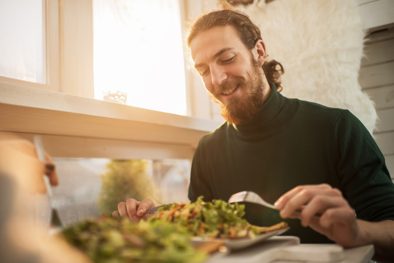 Happy man sitting at the restaurant and having salad for lunch.