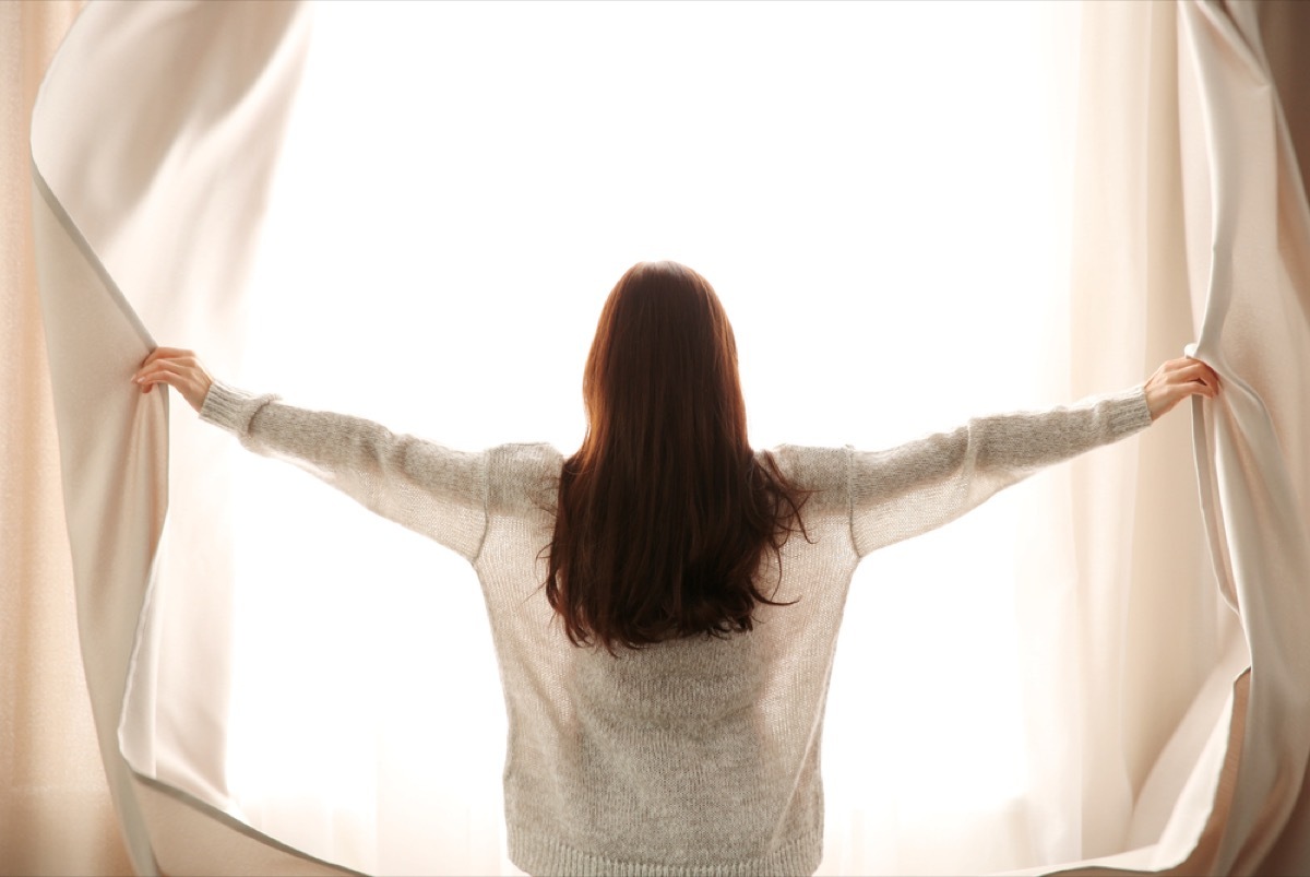 woman opening window curtains, property damage