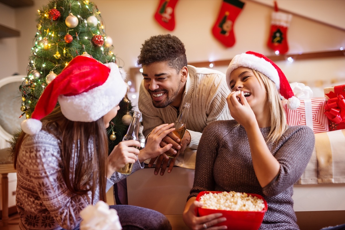 group of friends eating popcorn in front of the tree telling christmas jokes