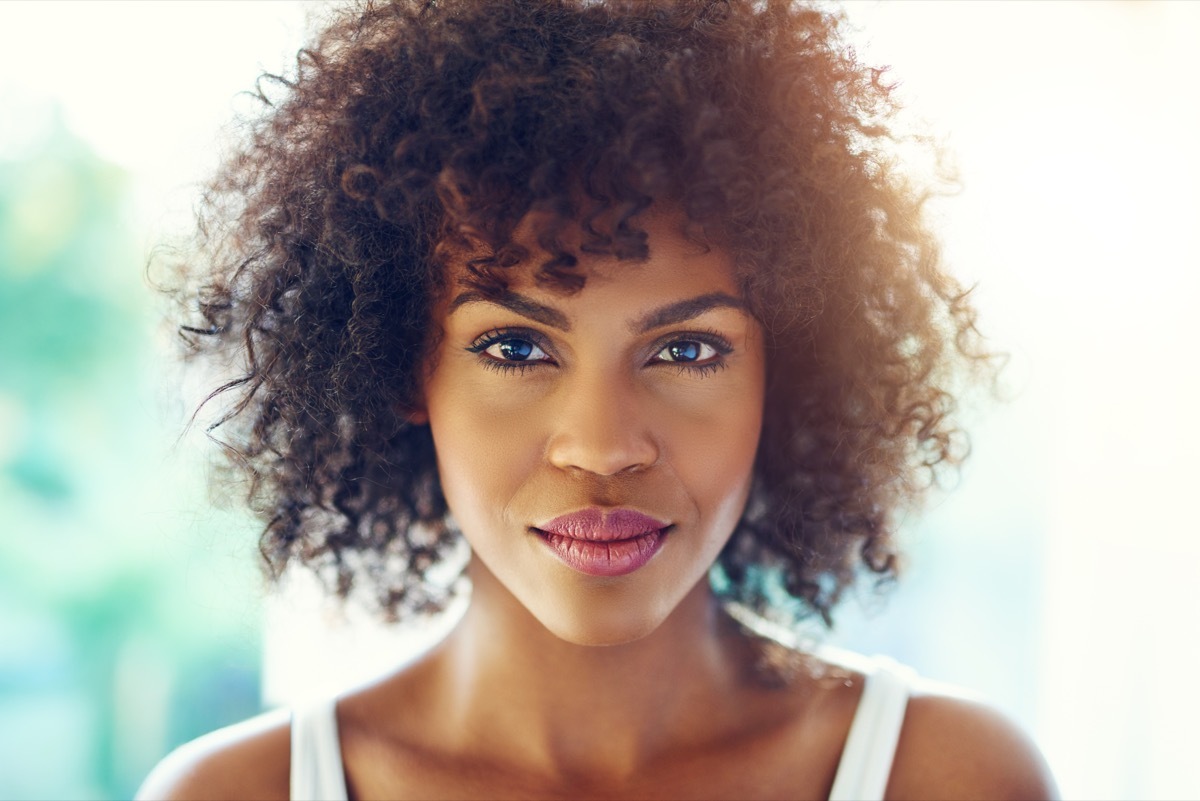 Portrait of young afro-american pretty girl looking at camera on blurred inside background.