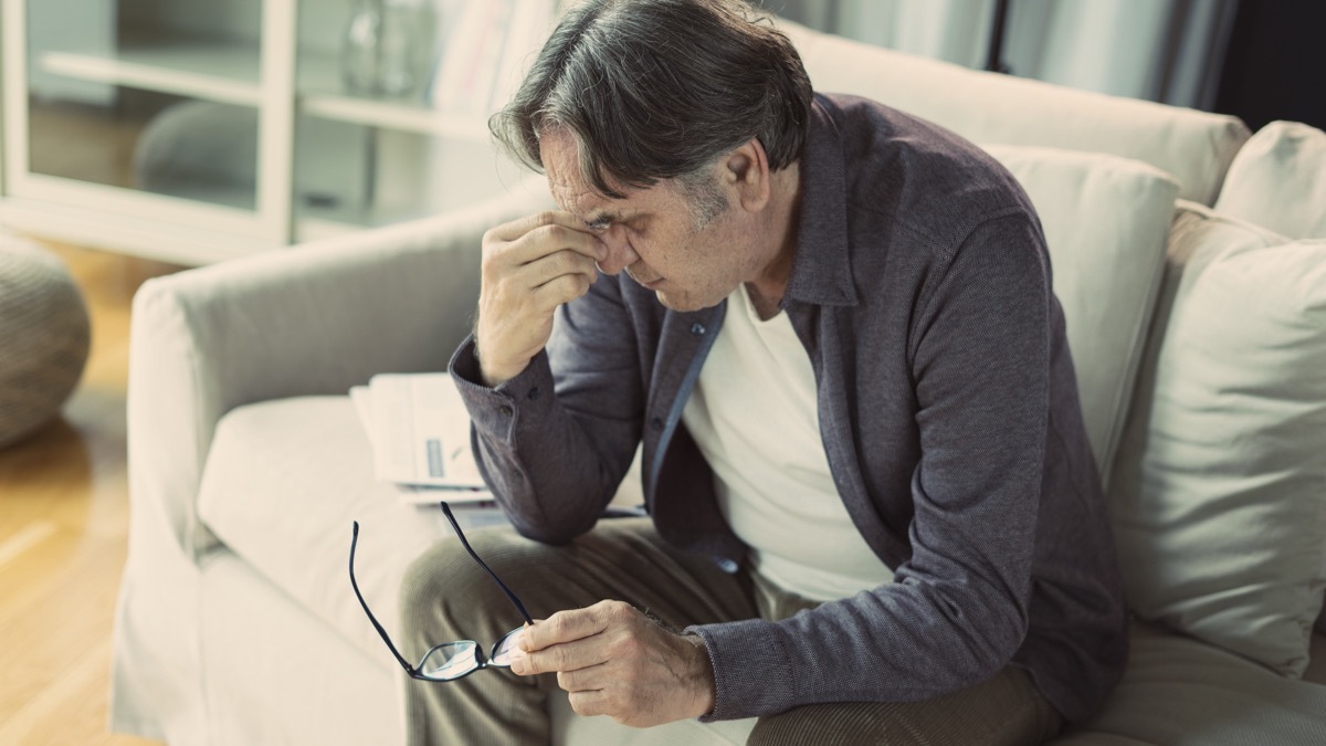 Man sitting on the couch holding his temples feeling stressed