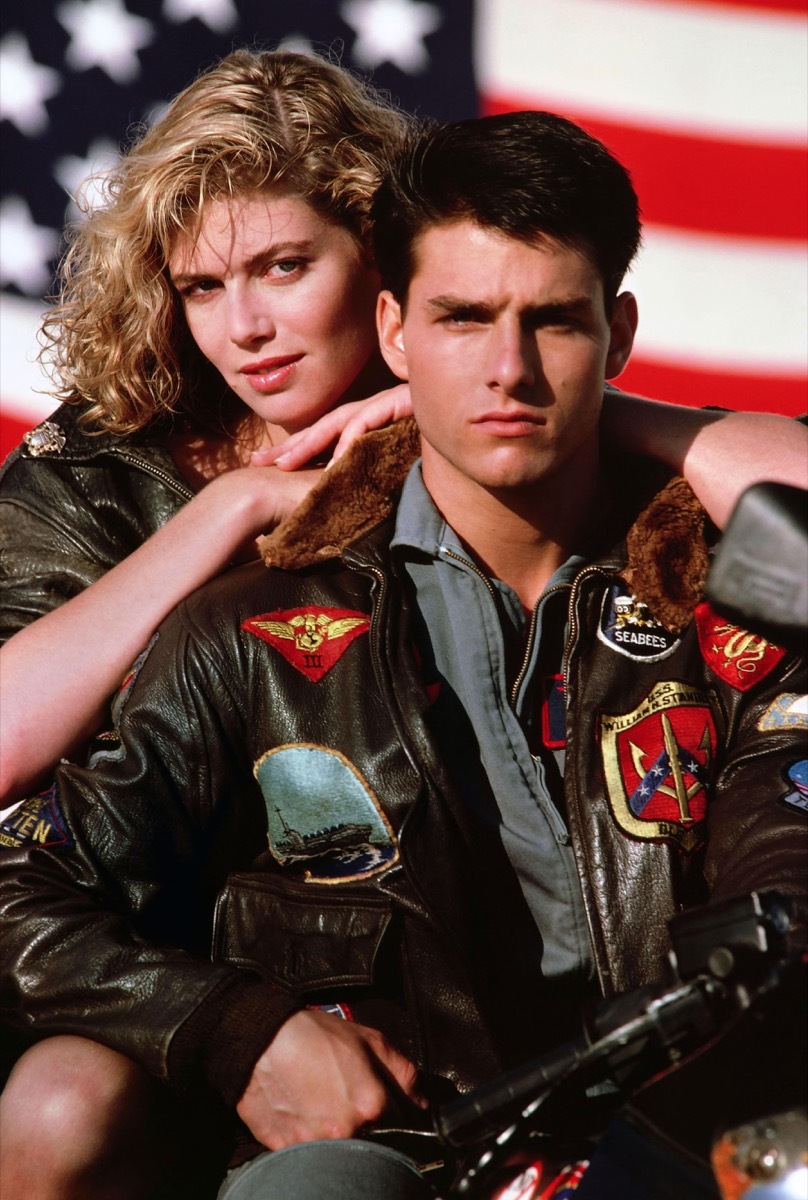 Tom Cruise in bomber jacket with Kelly McGillis leaning on his back in Top Gun movie, Cruise wears a '90s fashion trend