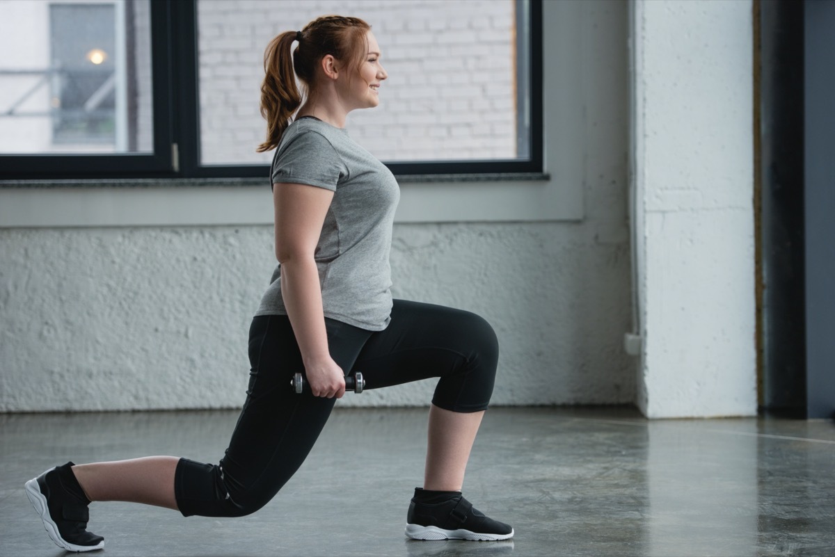 Plus size woman performing lunges with dumbbell in gym