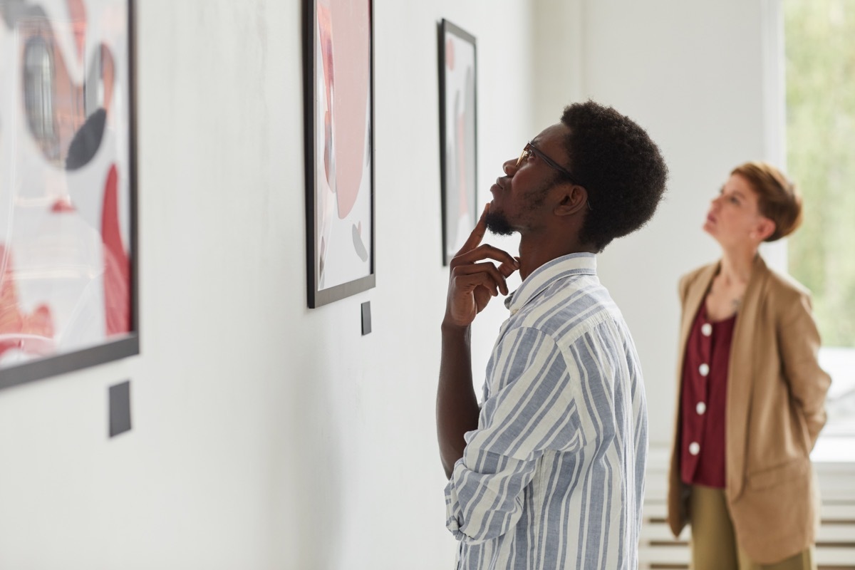 Side view portrait of young African-American man looking at paintings while exploring modern art gallery exhibition