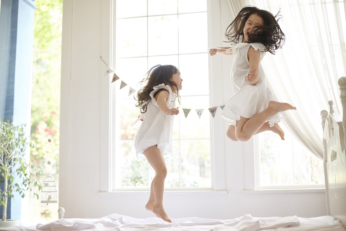 two young asian girls jumping on bed