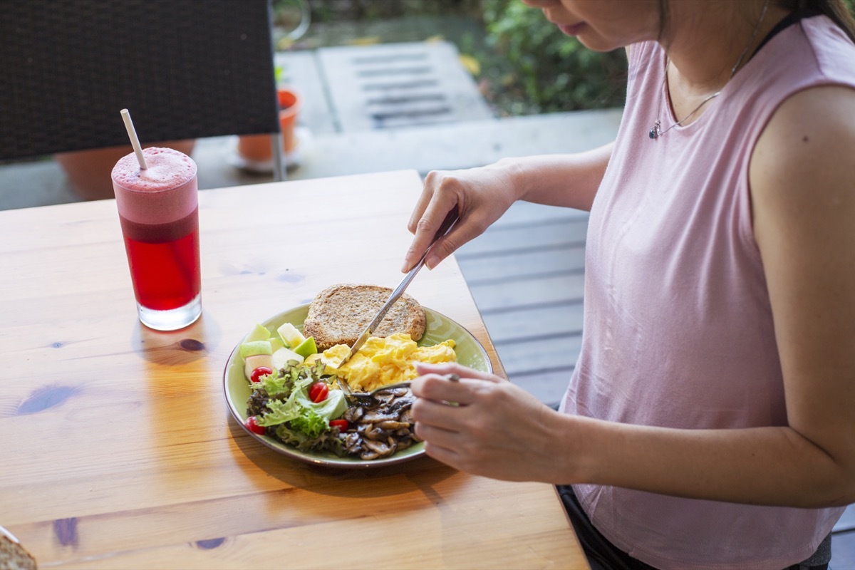 unrecognized woman eating healthy homemade breakfast with salad at backyard garden