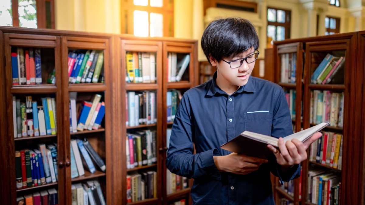 asian man reading the dictionary in a library