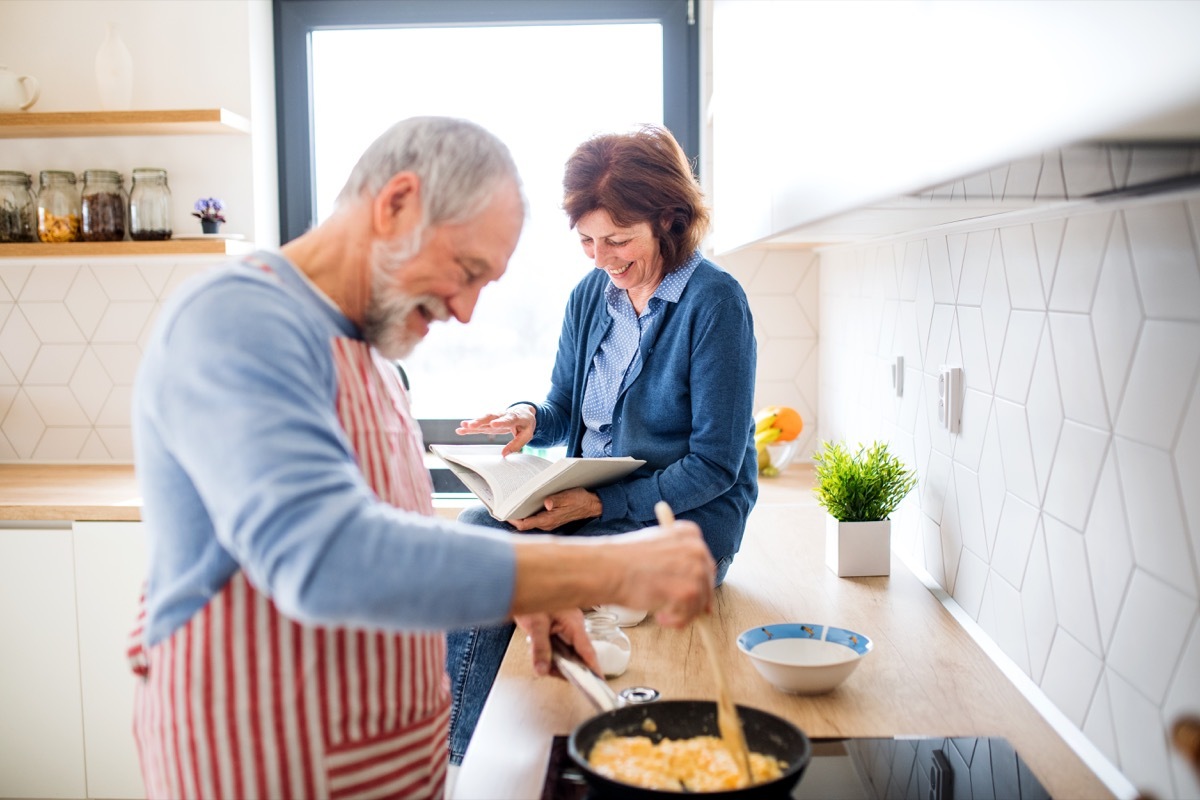 A portrait of happy senior couple in love indoors at home, cooking.