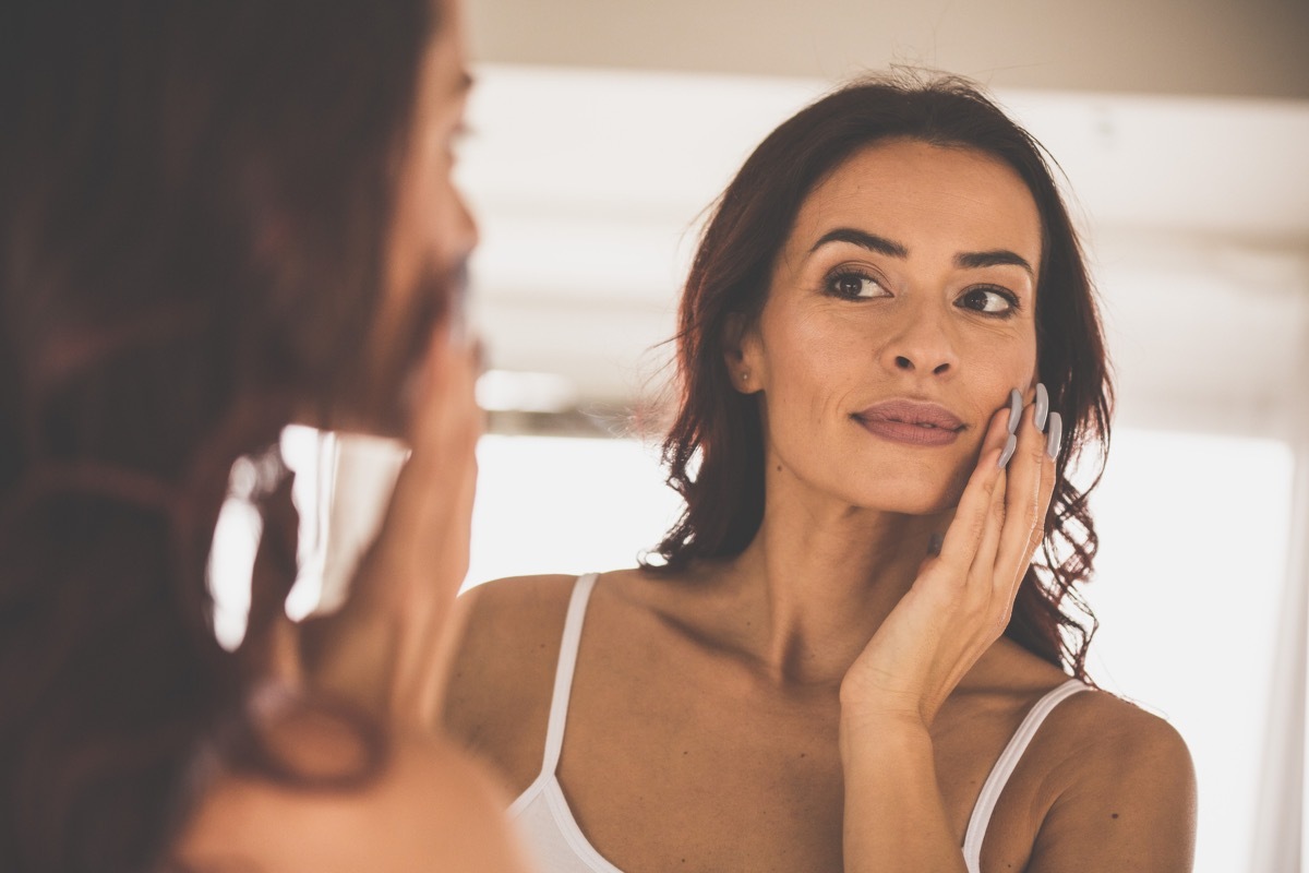 Woman with dry skin moisturizing her face in the mirror