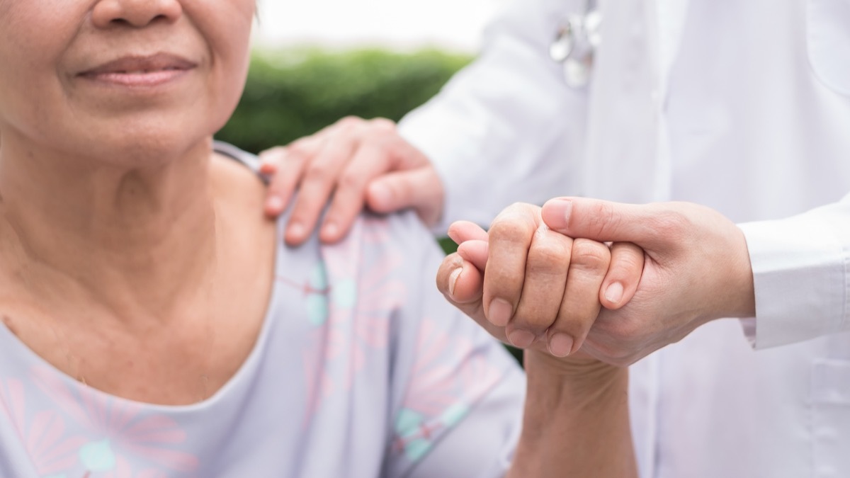 Elderly senior dementia patient in nursing hospice home holding geriatrician doctor's hand