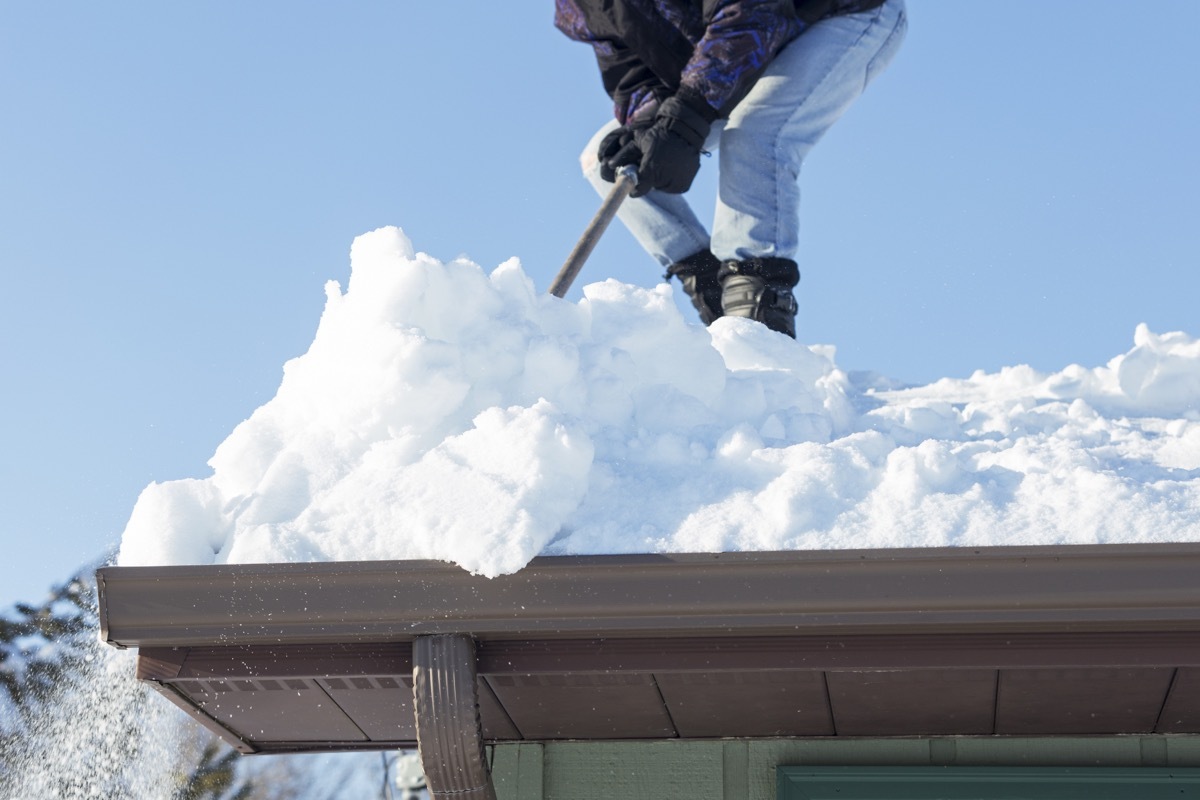 man scraping snow off roof