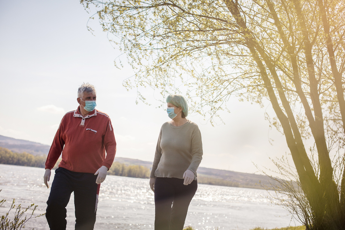 Senior couple walking trough nature with mask on face.