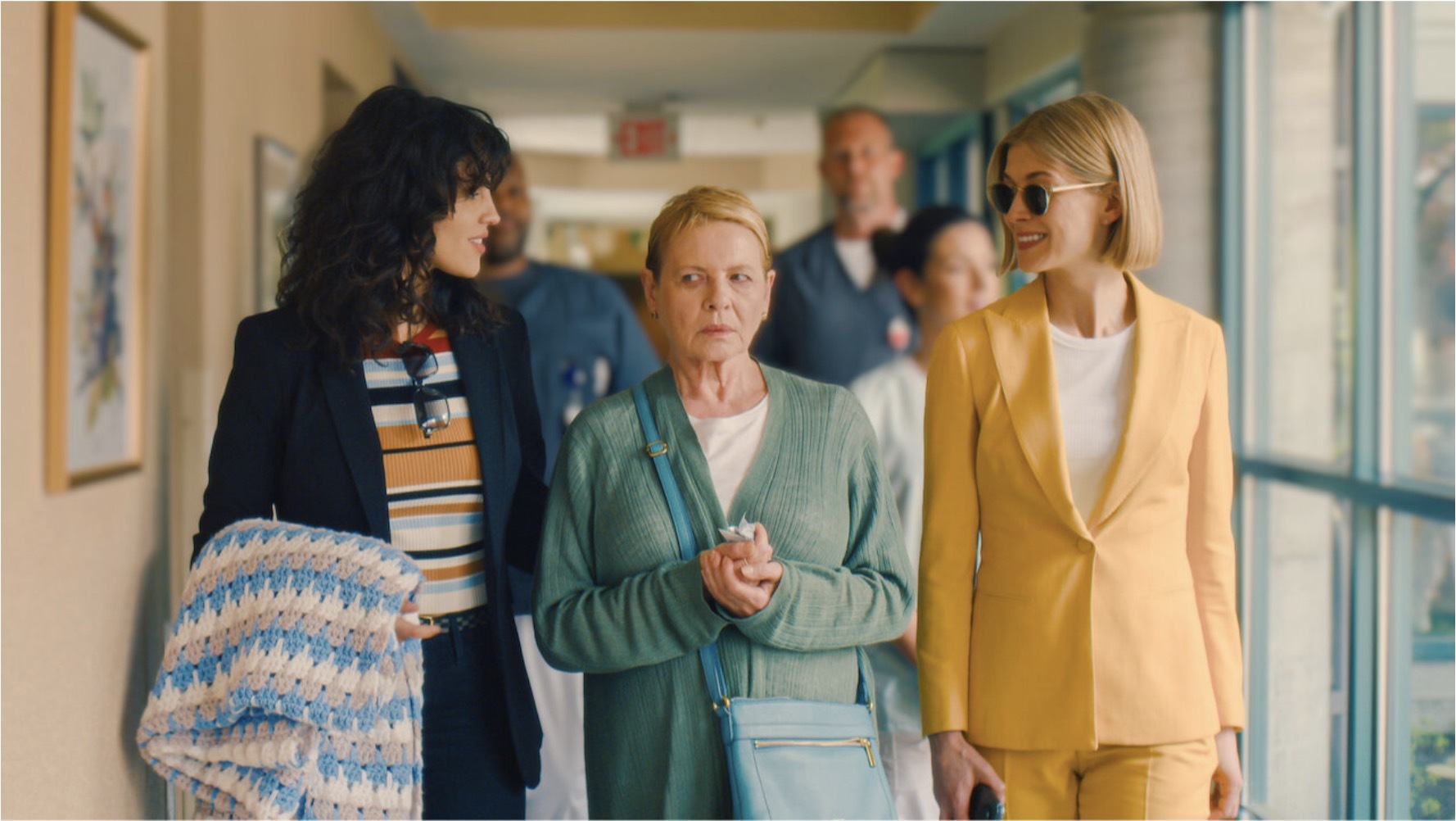 Two younger women walking an older woman down a hallway in a scene from I Care A Lot