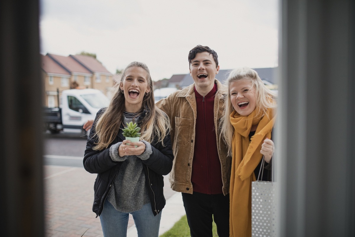 A point of view shot of a small group of friends arriving at a housewarming party, they have brought gifts for their host.