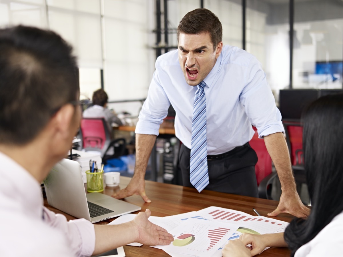 bad-tempered caucasian business executive yelling at two asian subordinates in office