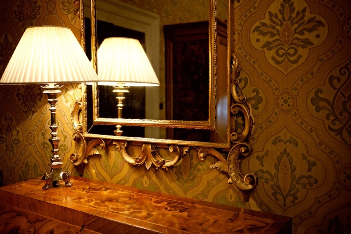 old fashioned lamp in front of gilded mirror on credenza