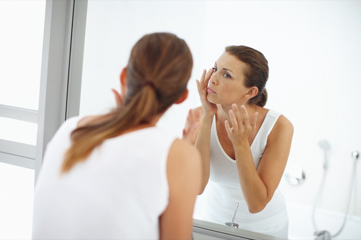 Woman applying lotion to the skin around her eyes in the mirror