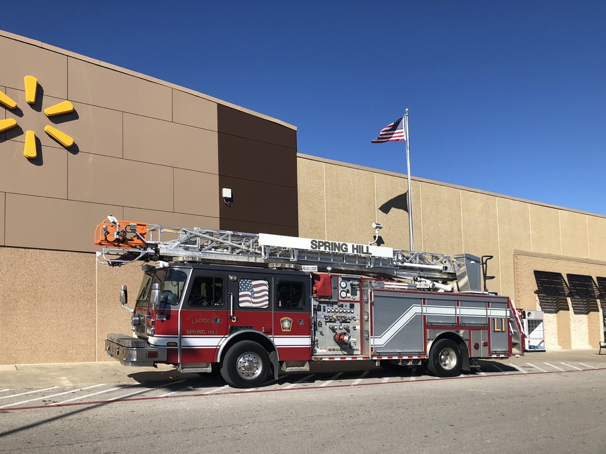 New, large ladder style fire truck in front of a Walmart with an American flag flying in the breeze.