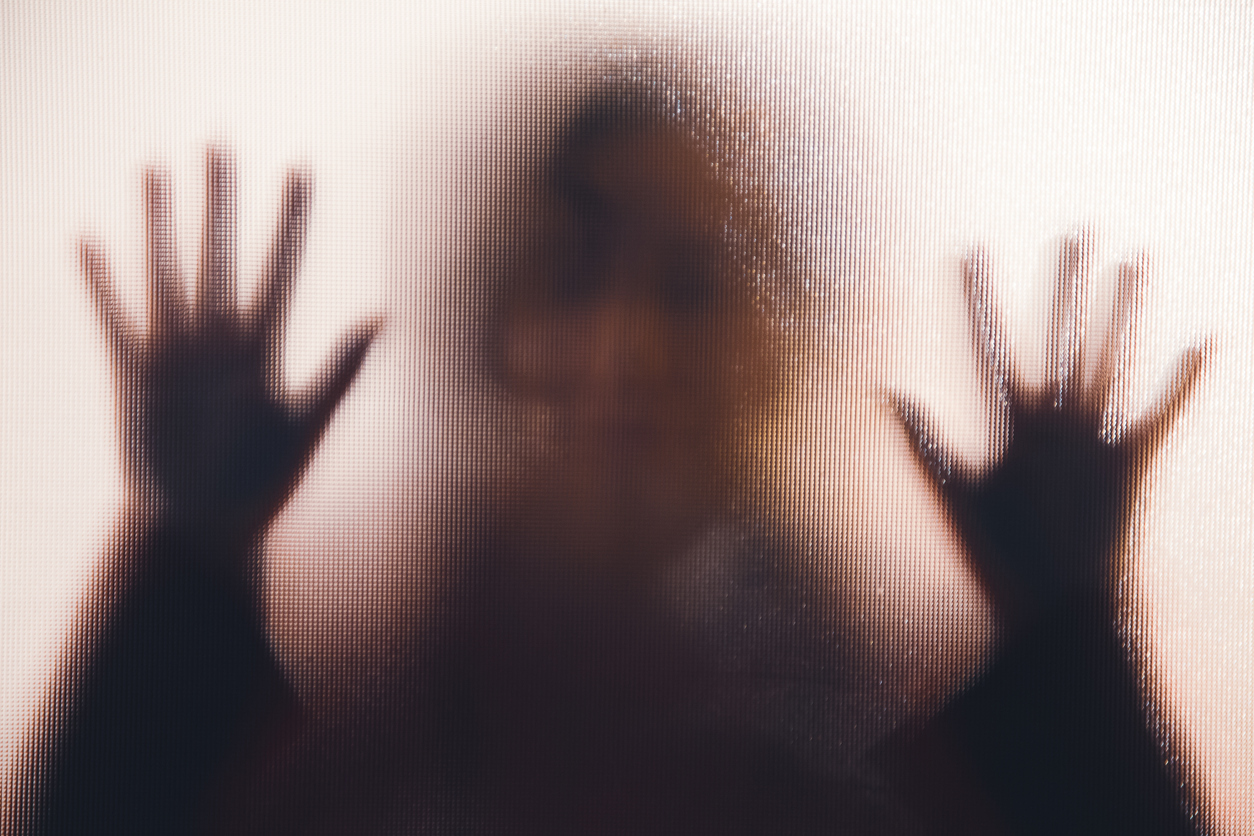 silhouette of a woman with her hands pressed against a glass window.