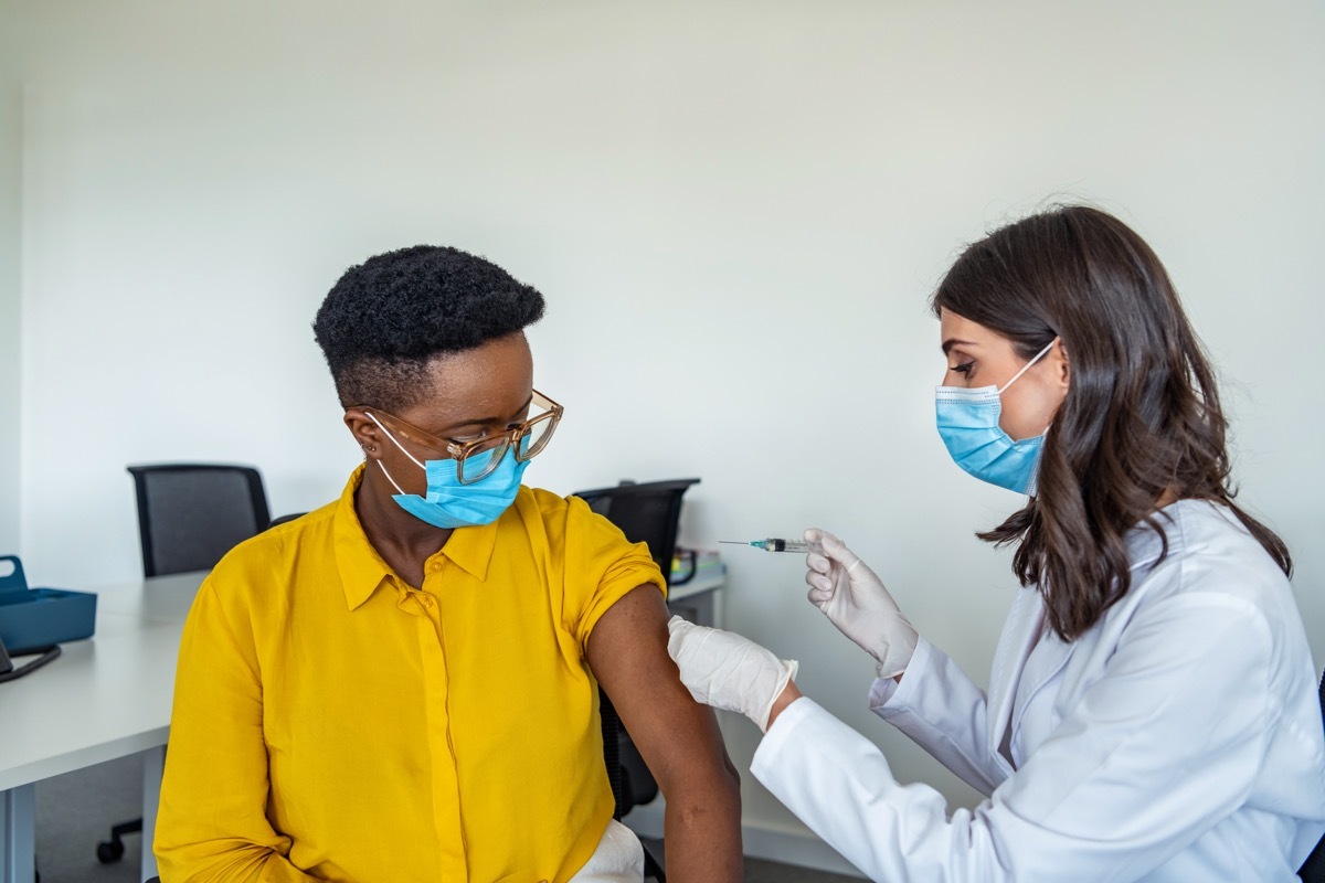 Mid adult woman in medical face mask getting Covid-19 vaccine at doctor's office.