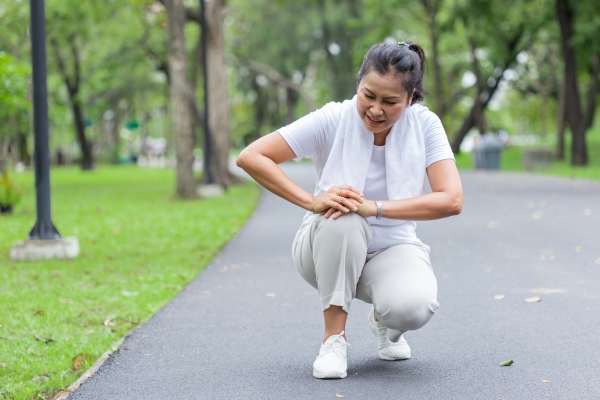 woman kneeling in pain, outside in park