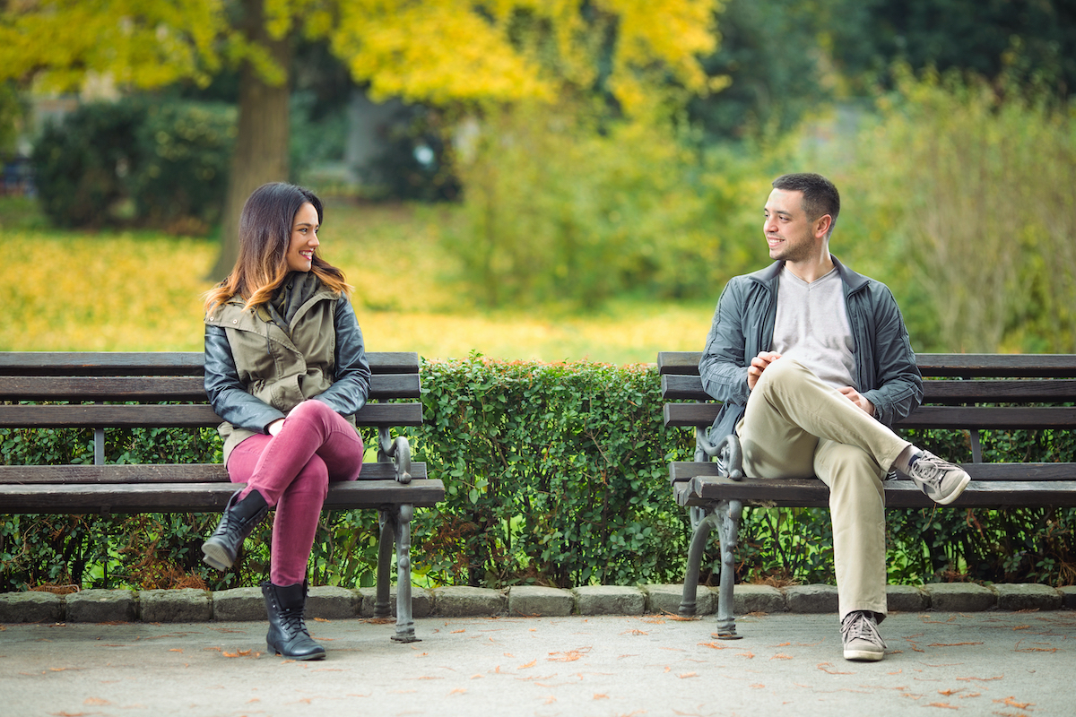 Two young people sitting on benches in a park and talking