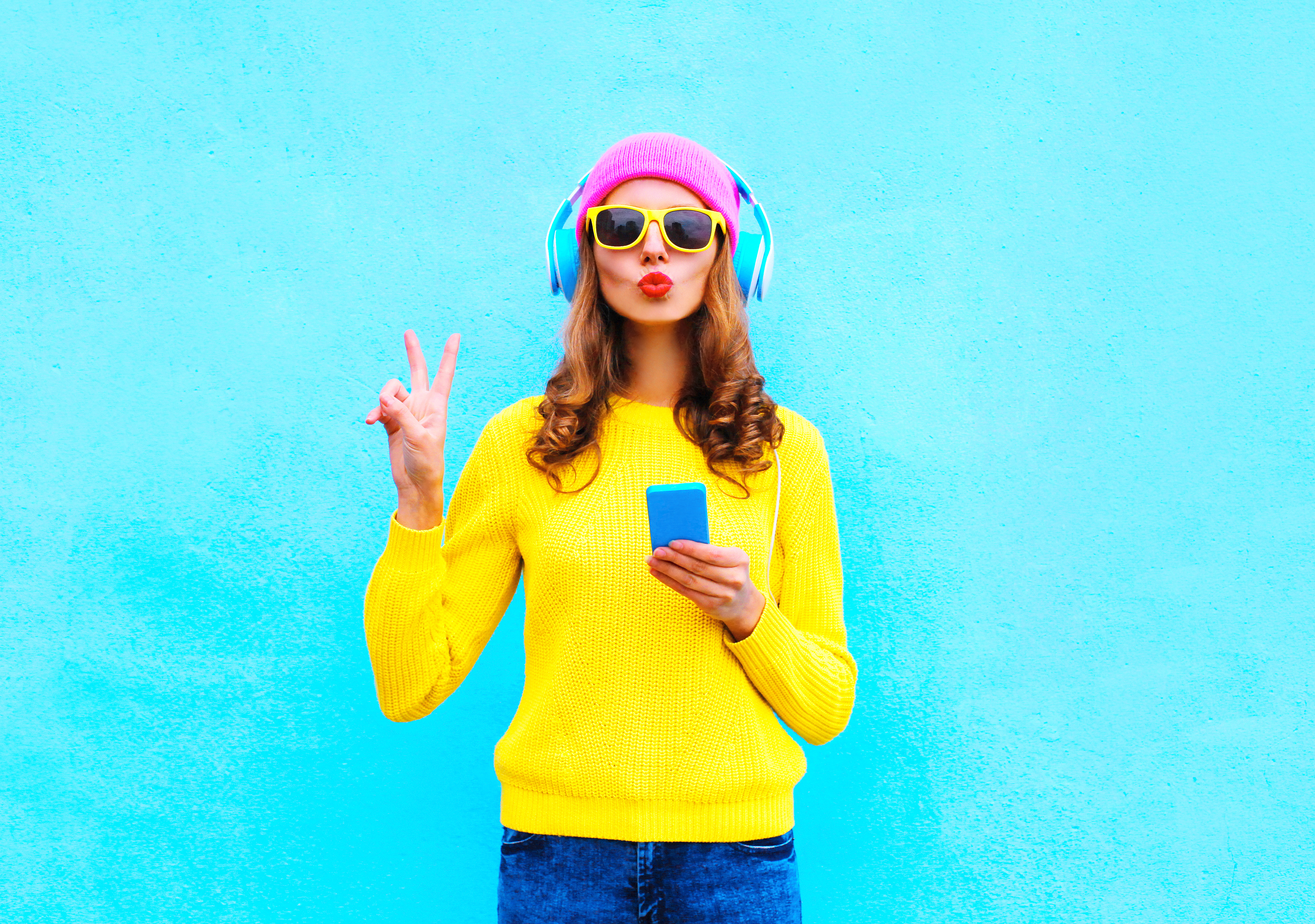 woman in hat and headphones taking a selfie while giving the peace sign