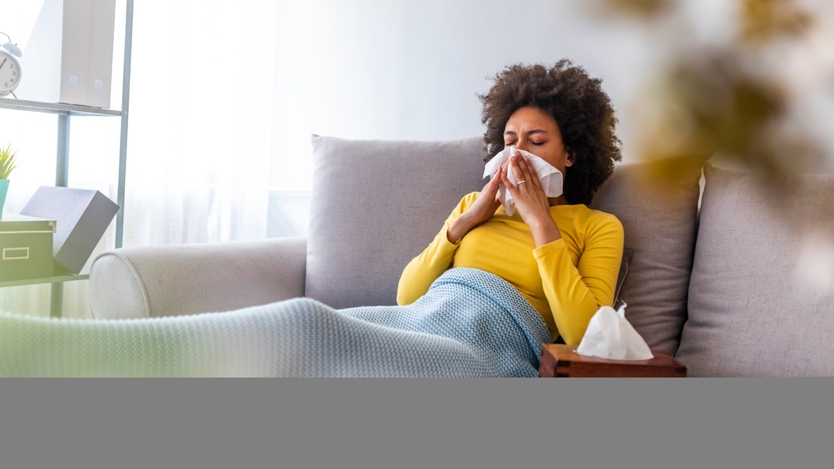 Woman on couch blowing nose sick at home