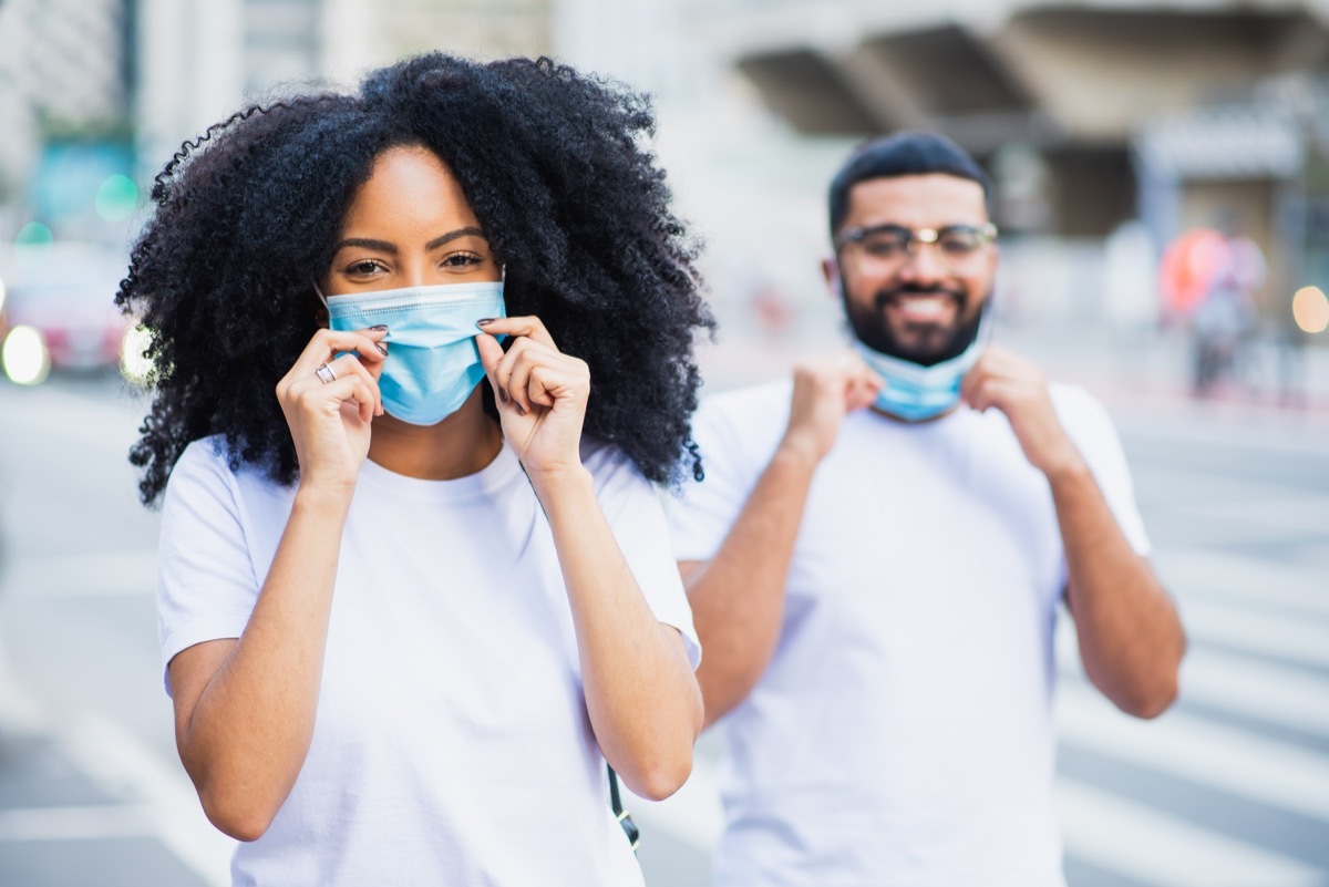 Two young people smiling in the city and removing / putting on face protection mask