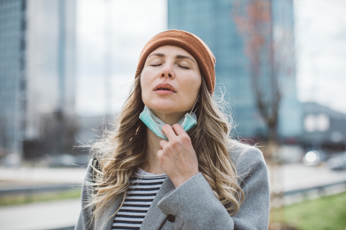 Woman removing face mask from her face outdoors.