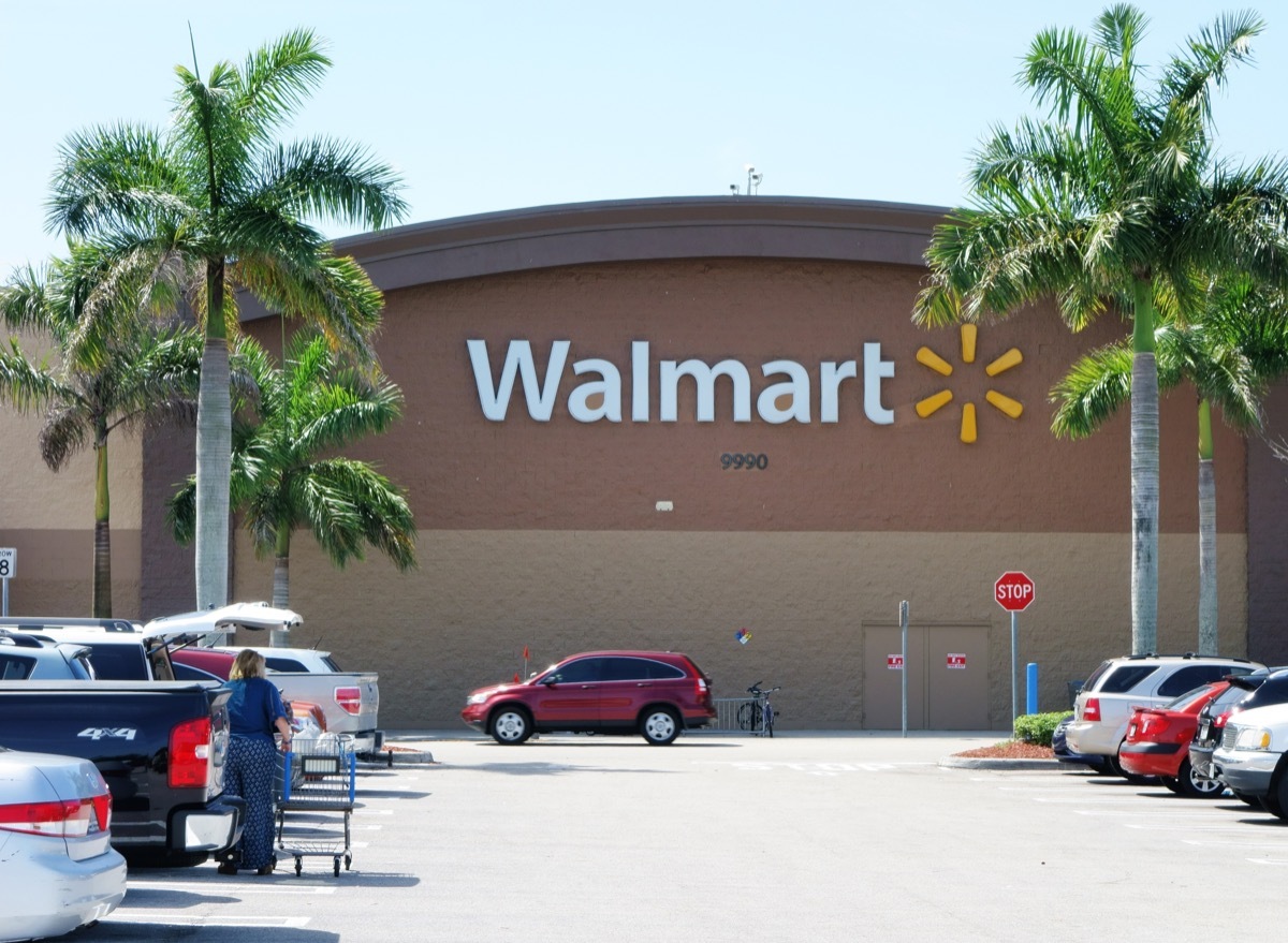 A Walmart store with a full parking lot. Walmart is the largest retailer in the world and operates thousands of large discount department stores. A woman customer empties her shopping cart into a car in the parking lot.