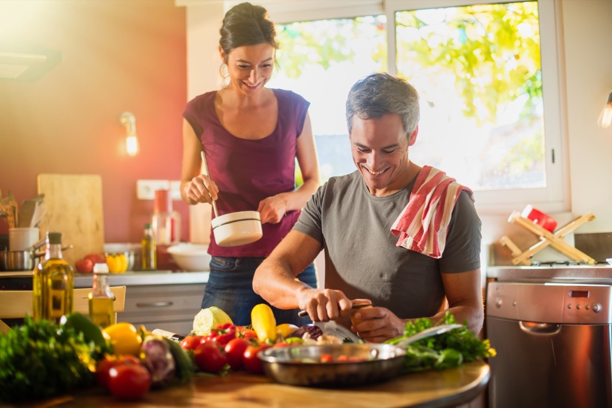 Trendy couple cooking vegetables from the market in a red kitchen