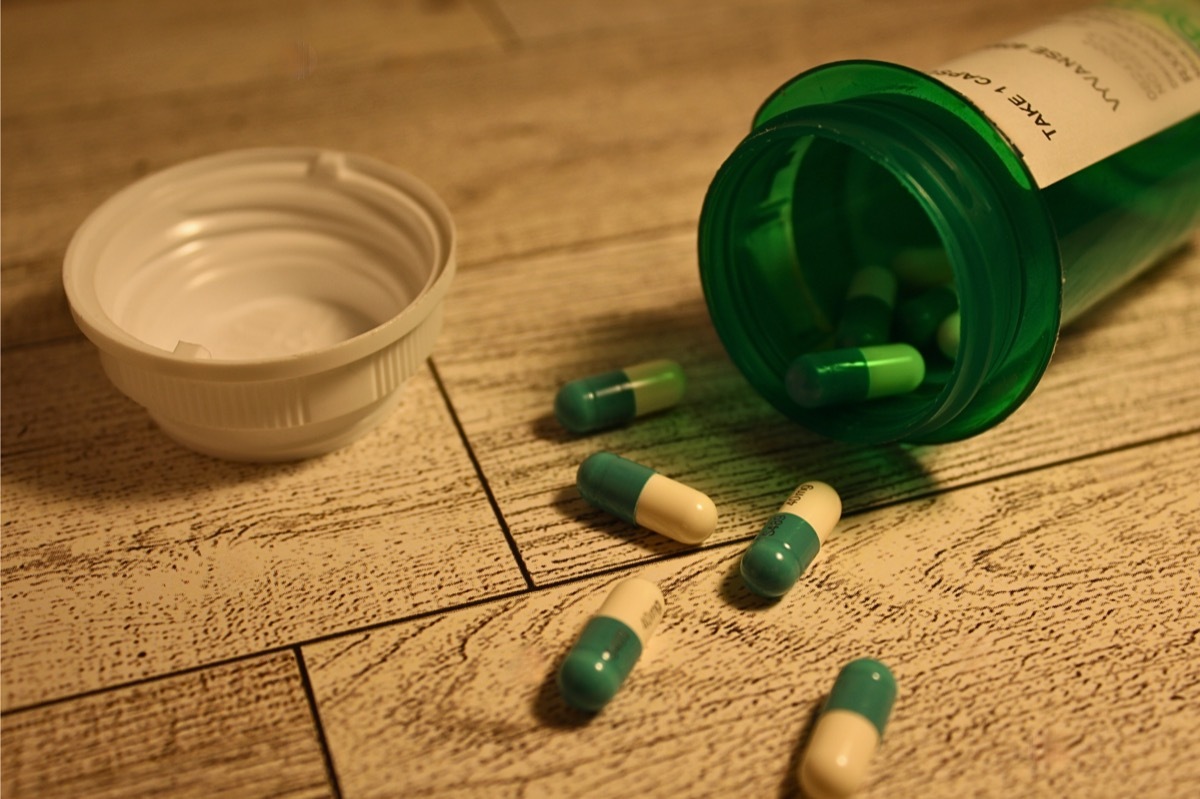 Spilled green pill bottle with Vyvanse medication on a grey toned wooden floor.