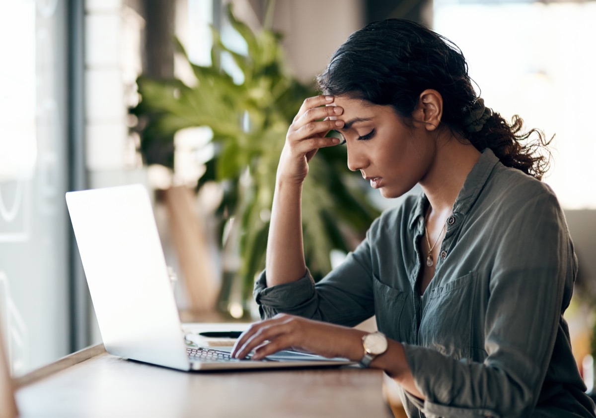 Shot of a young woman experiencing stress while working in a cafe