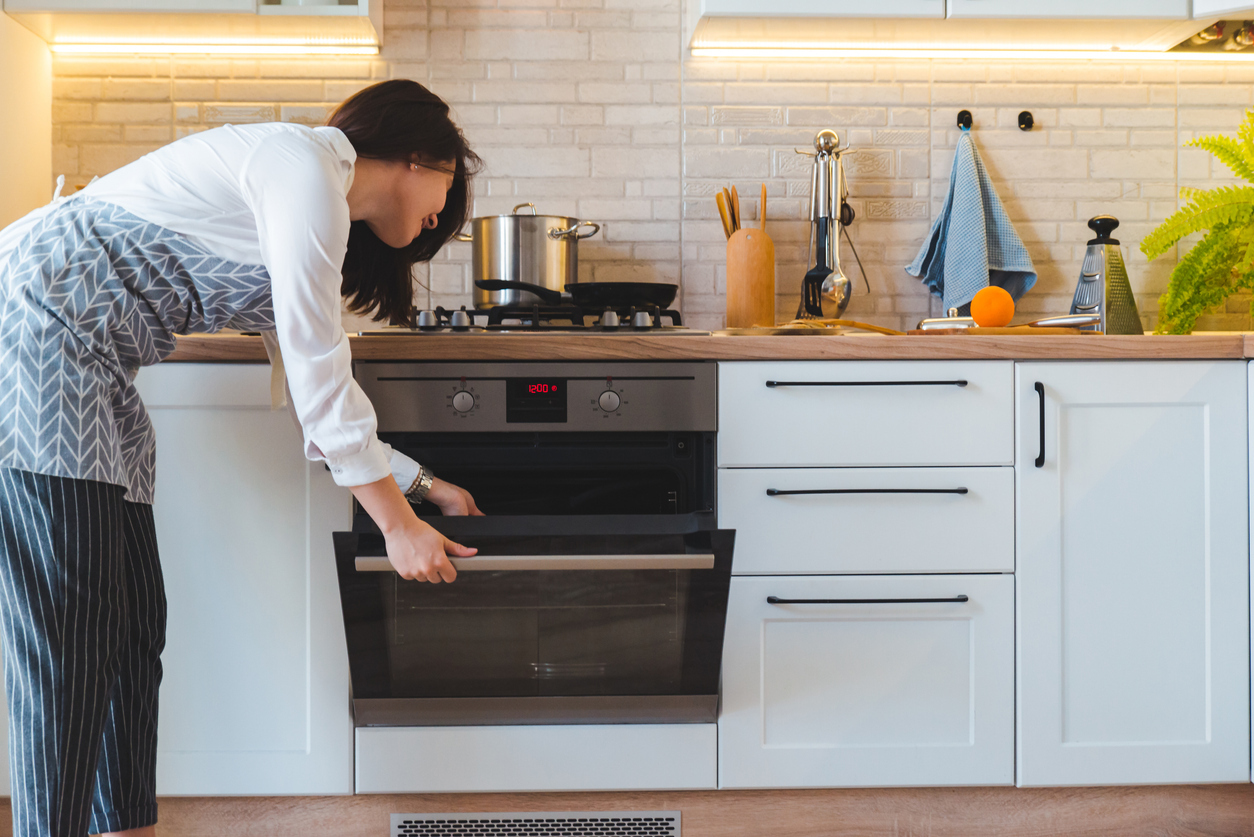 A woman wearing an apron checks inside the oven in her kitchen