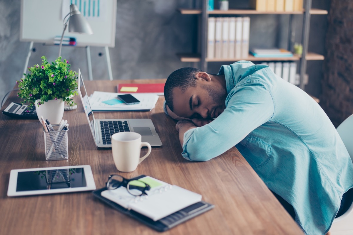 a man sleeping at a desk with a laptop computer and a tablet in front of him