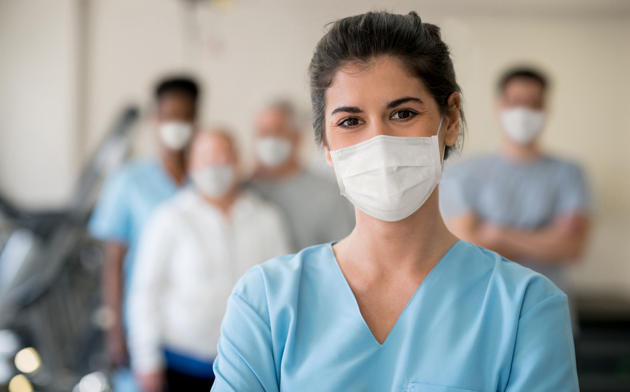 A young woman wearing a face mask with a group of others wearing face masks standing in the background.