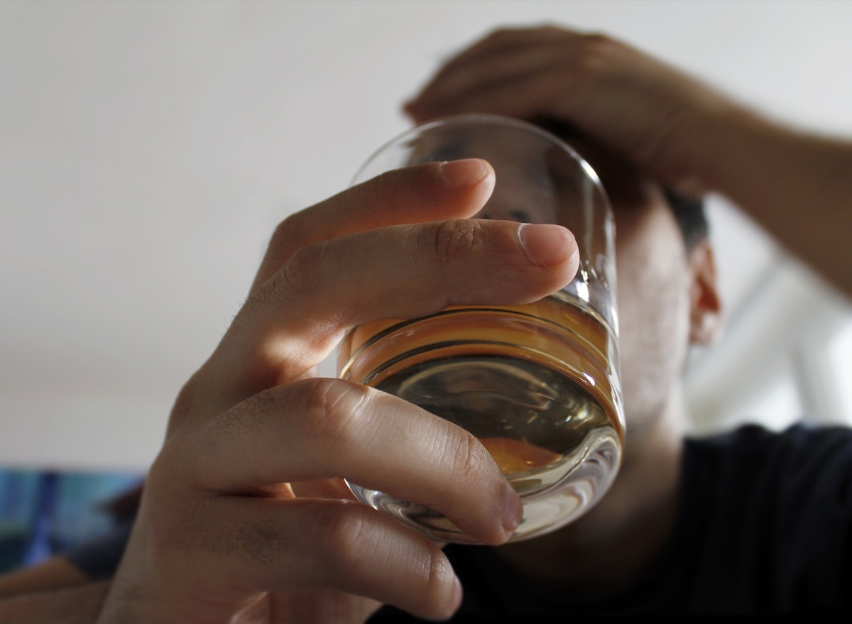 Young man holding glass of alcohol with hand on head, shot from below the glass up at his face