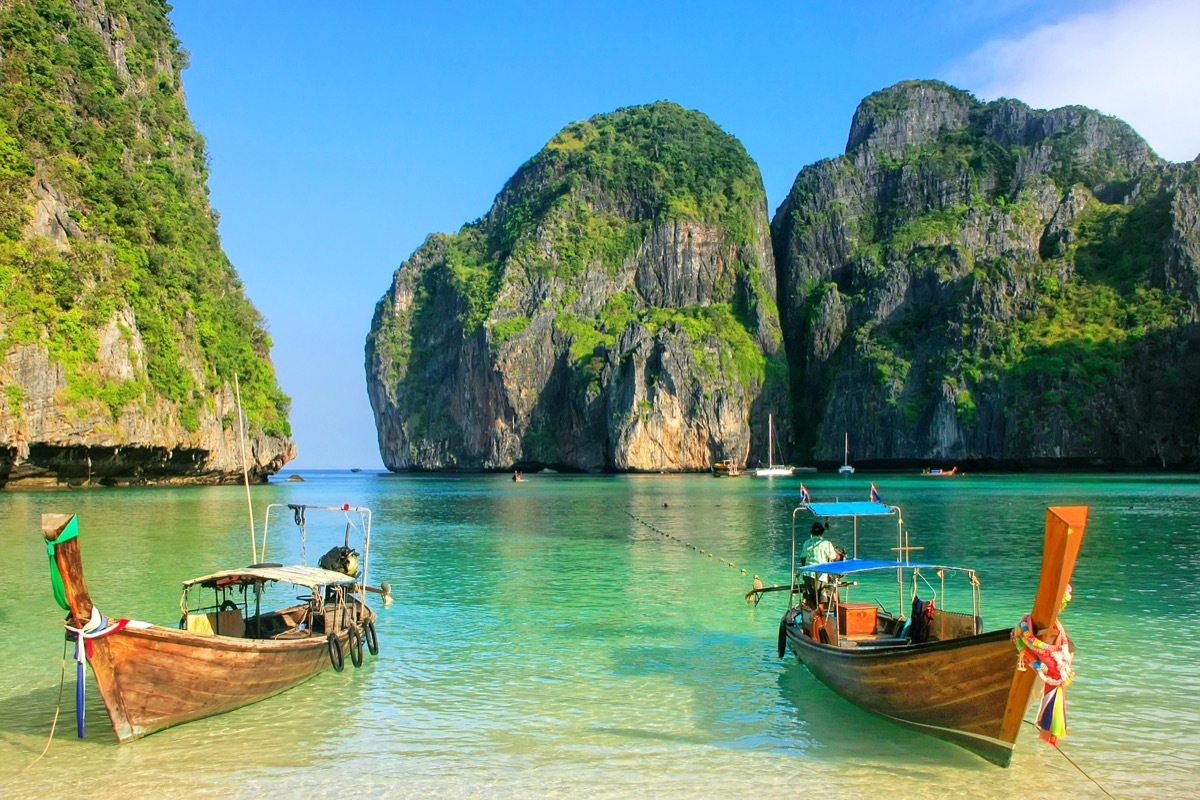 boats on a shore with cliffs jutting out of a bay in the background