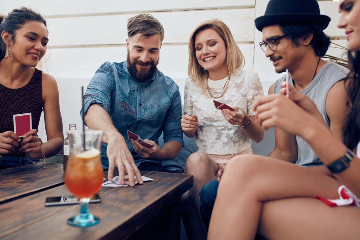 Group of friends relaxing and playing cards together. Young people hanging out together around a table during a party playing a game of cards.