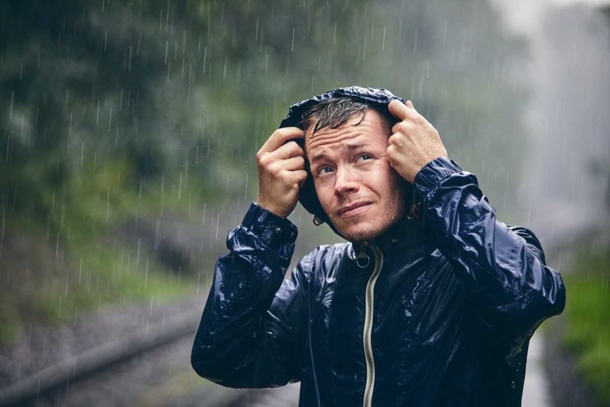 Trip in bad weather. Portrait of young man in drenched jacket in heavy rain.