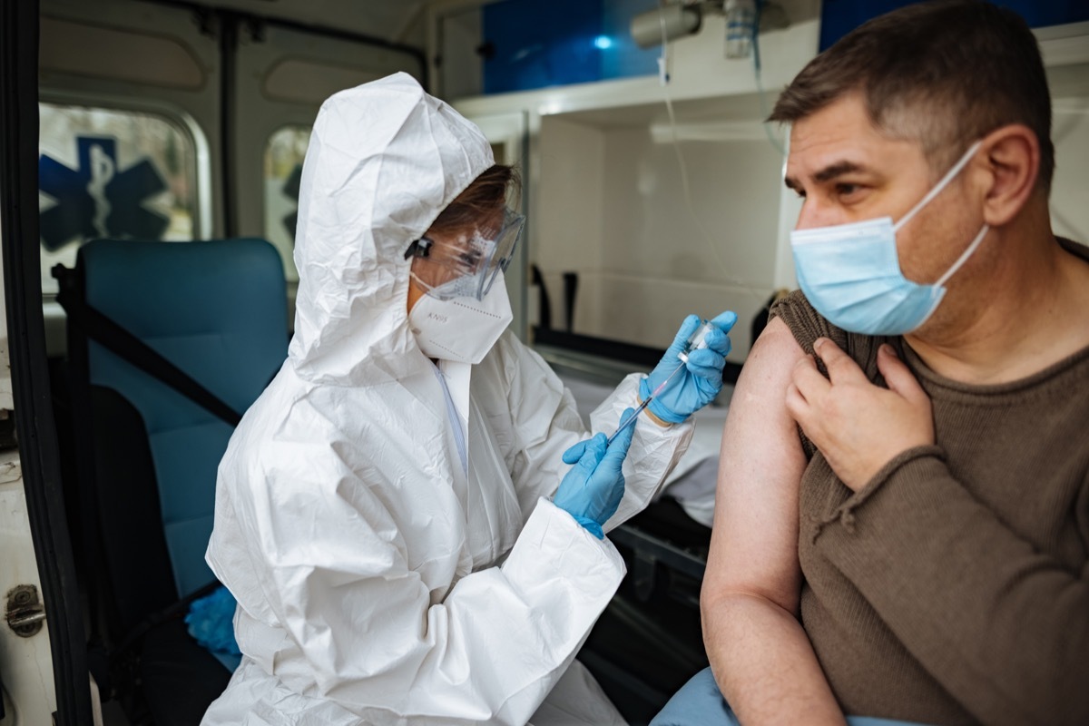 Female doctor injecting COVID-19 vaccine into patients arm with syringe