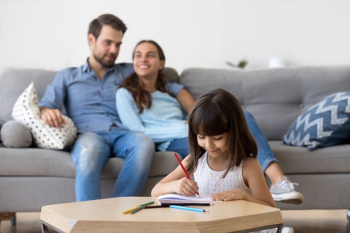 Young girl drawing while parents are relaxing and talking