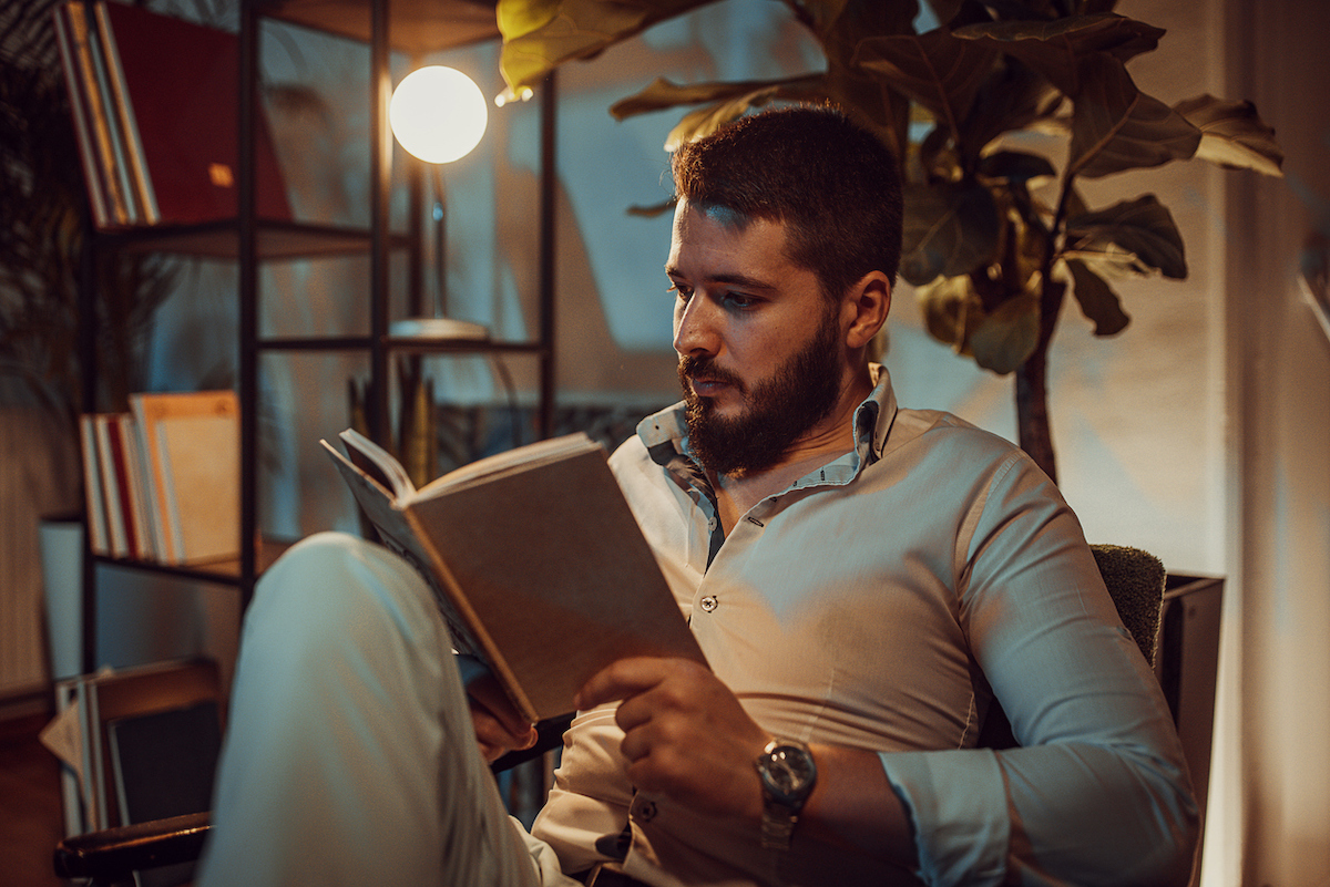 Man sitting on a chair and reading a book at home at night.