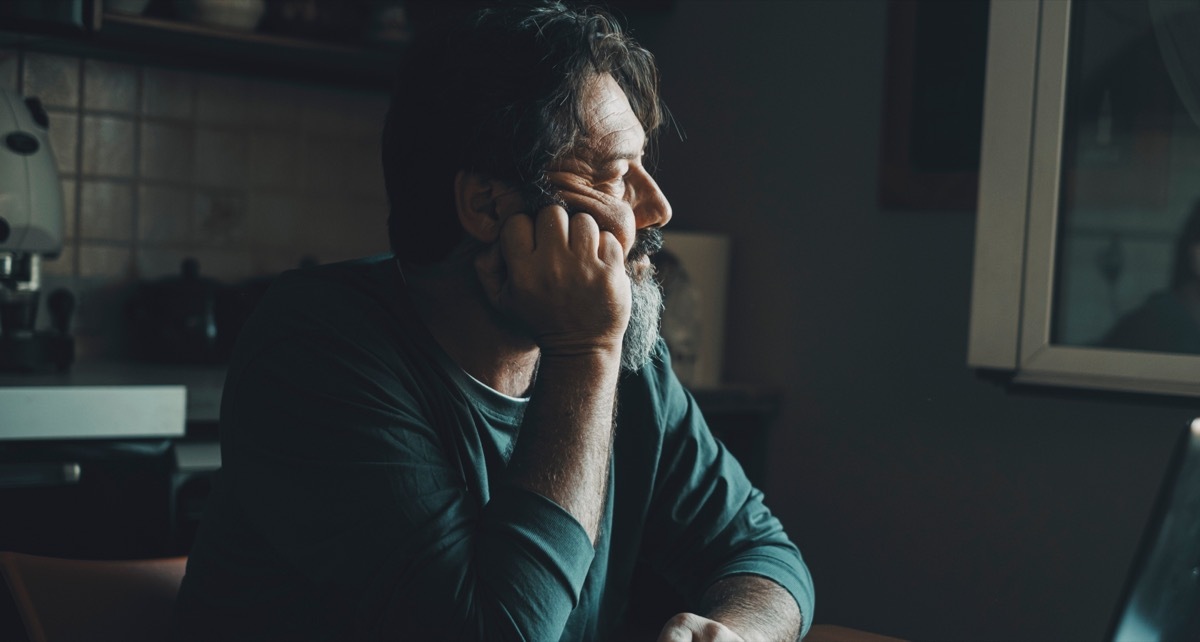 older man sitting at home in the dark looking thoughtful