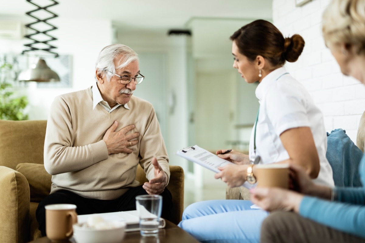 Mature man communicating with female doctor and complaining of chest pain during home visit.